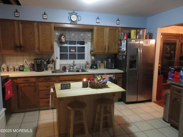 kitchen with tasteful backsplash, a center island, sink, stainless steel fridge with ice dispenser, and light tile patterned floors