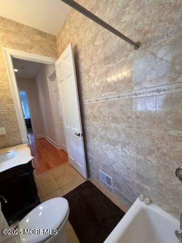 bathroom with tile patterned flooring, vanity, toilet, and tile walls