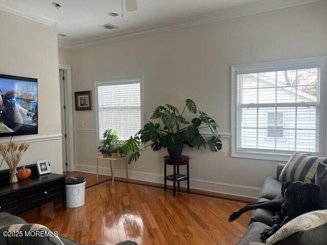 living room with ceiling fan, wood-type flooring, ornamental molding, and a wealth of natural light