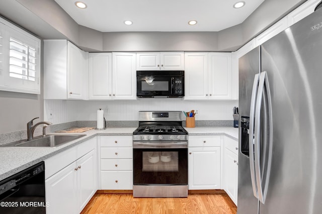 kitchen with sink, white cabinetry, black appliances, and light hardwood / wood-style flooring