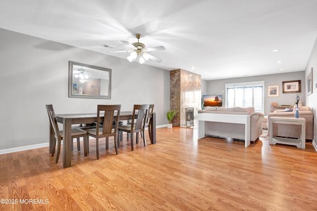 dining area with a fireplace, light hardwood / wood-style flooring, and ceiling fan