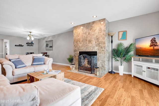 living room featuring light wood-type flooring, ceiling fan, and a large fireplace