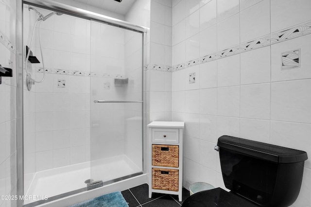 bathroom with tile patterned floors, toilet, tile walls, and a shower with door