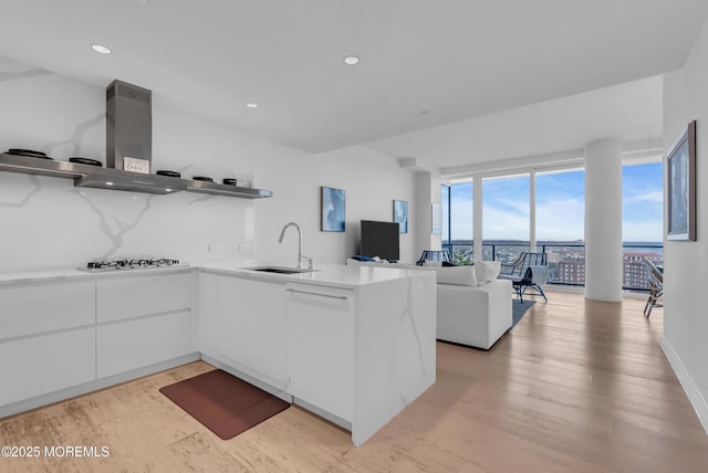 kitchen with sink, wall chimney exhaust hood, white gas stovetop, kitchen peninsula, and white cabinets