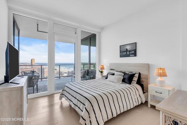 bedroom featuring floor to ceiling windows, access to exterior, light hardwood / wood-style floors, and a water view