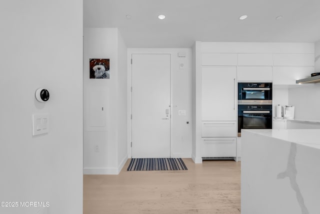 kitchen with double oven, white cabinetry, and light hardwood / wood-style floors