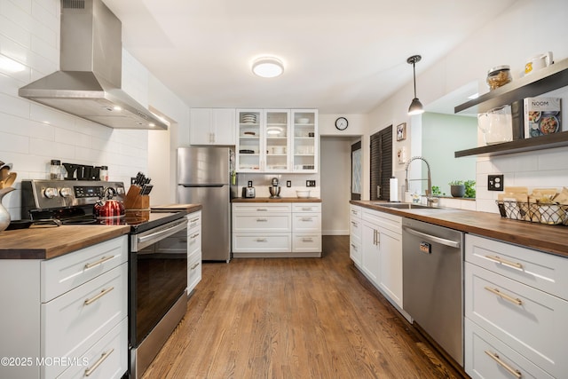 kitchen featuring ventilation hood, stainless steel appliances, hanging light fixtures, and wooden counters