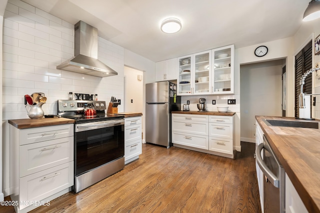 kitchen featuring backsplash, wall chimney range hood, stainless steel appliances, white cabinets, and wood counters