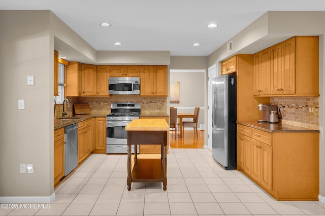 kitchen with sink, light tile patterned flooring, tasteful backsplash, light stone countertops, and appliances with stainless steel finishes