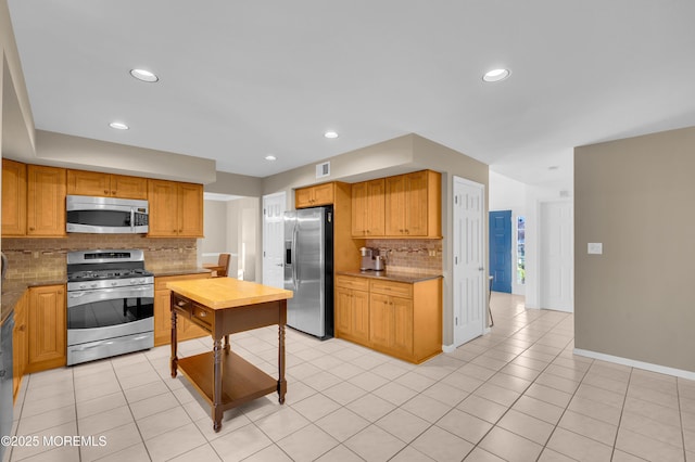 kitchen with stainless steel appliances, light tile patterned flooring, decorative backsplash, and light stone countertops