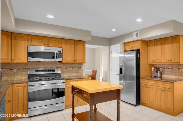 kitchen featuring dark stone counters, stainless steel appliances, decorative backsplash, and light tile patterned floors