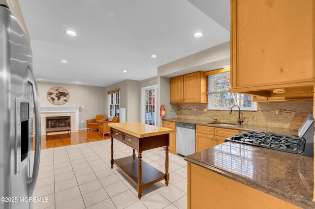 kitchen featuring dark stone countertops, appliances with stainless steel finishes, light tile patterned floors, sink, and backsplash