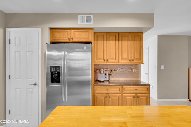 kitchen with light stone countertops, light tile patterned floors, backsplash, and stainless steel fridge