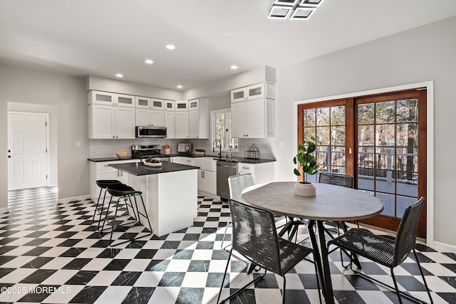 kitchen with stainless steel appliances, a kitchen island, a breakfast bar area, white cabinetry, and sink