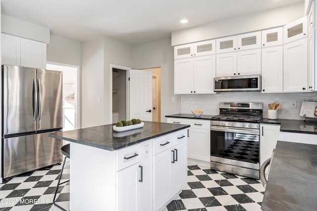 kitchen with white cabinets, decorative backsplash, a kitchen island, a breakfast bar, and appliances with stainless steel finishes