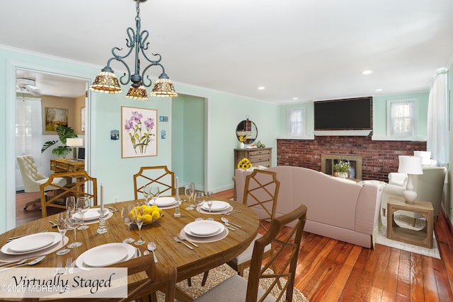 dining room with hardwood / wood-style flooring, a notable chandelier, a brick fireplace, and crown molding