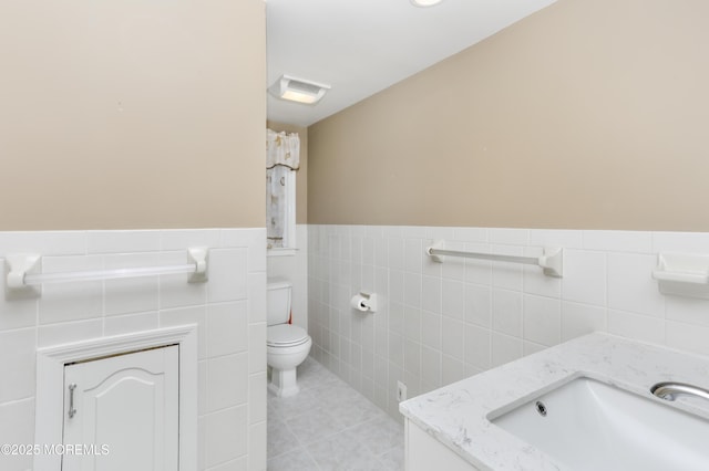 bathroom with toilet, tile patterned floors, vanity, and tile walls