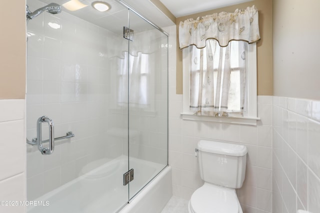 bathroom with toilet, combined bath / shower with glass door, and tile walls