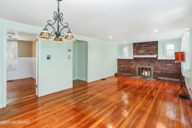 unfurnished living room with a brick fireplace, ornamental molding, a chandelier, and hardwood / wood-style floors