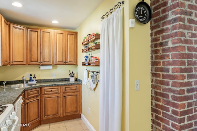 kitchen with sink, white range with gas stovetop, light tile patterned floors, and dark stone counters