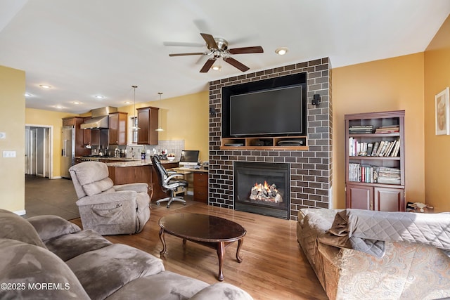 living room with ceiling fan, a large fireplace, and dark wood-type flooring