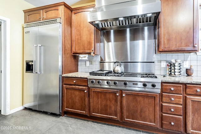 kitchen featuring decorative backsplash, light stone counters, range hood, and appliances with stainless steel finishes