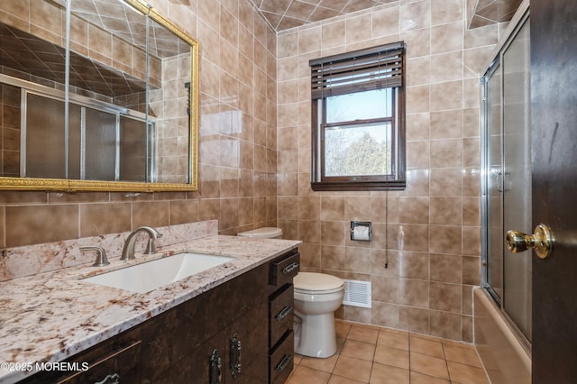 full bathroom with toilet, vanity, tile patterned flooring, tile walls, and shower / bath combination with glass door