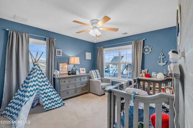 carpeted bedroom with ceiling fan and a nursery area