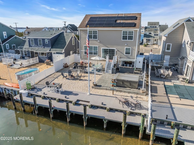 rear view of house featuring a jacuzzi, a water view, a patio, and solar panels