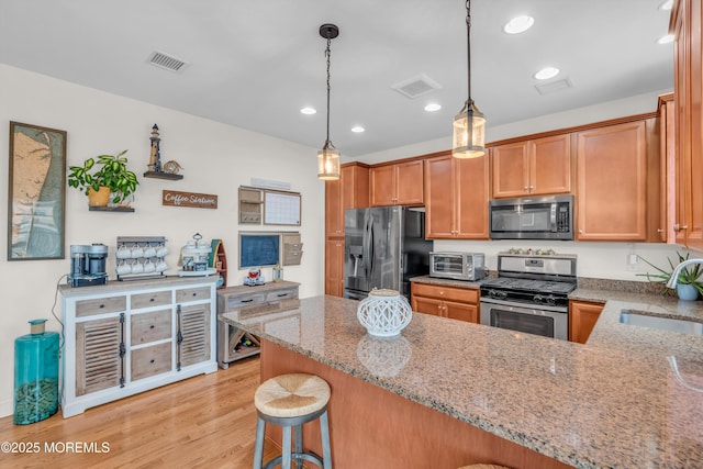 kitchen with sink, light stone countertops, appliances with stainless steel finishes, kitchen peninsula, and a breakfast bar area