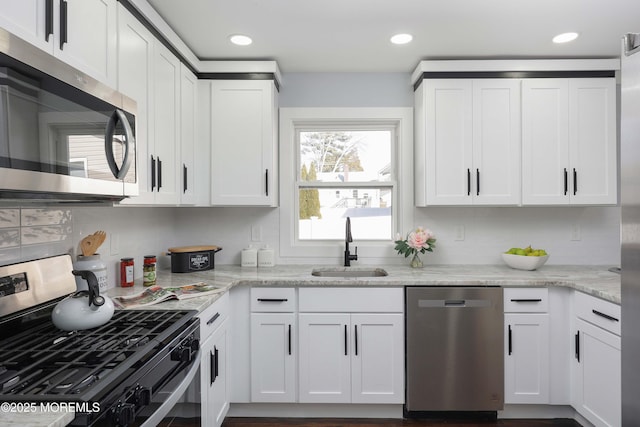 kitchen with stainless steel appliances, white cabinetry, light stone counters, and sink