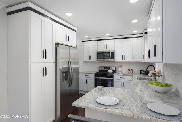 kitchen with white cabinetry, kitchen peninsula, appliances with stainless steel finishes, light stone countertops, and sink