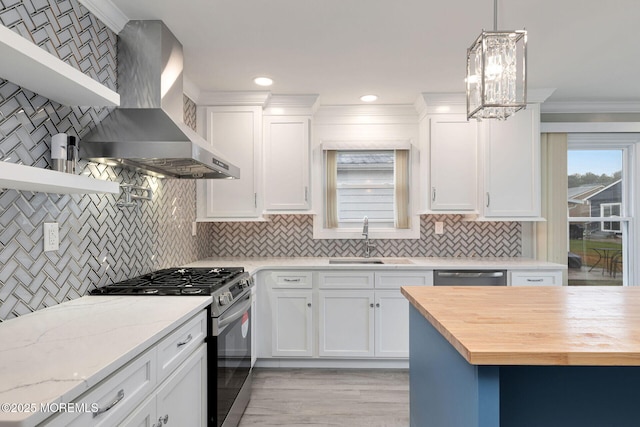 kitchen with light stone countertops, wall chimney exhaust hood, decorative light fixtures, white cabinetry, and appliances with stainless steel finishes