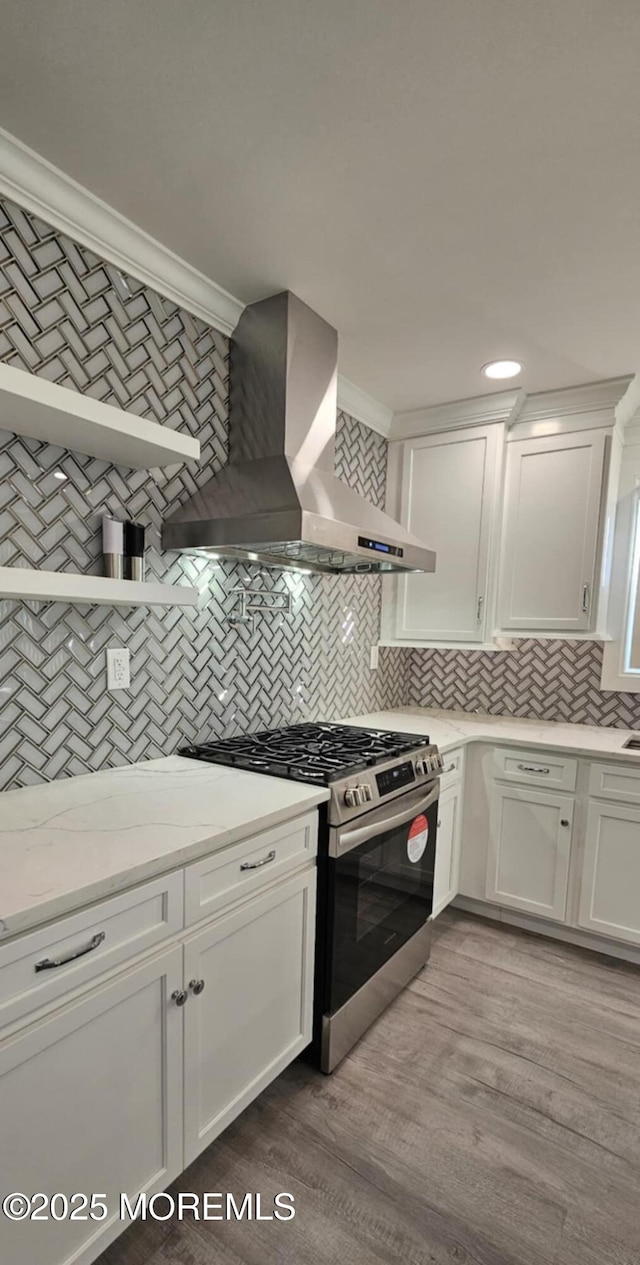 kitchen featuring stainless steel range with gas stovetop, wall chimney range hood, white cabinetry, and light stone countertops