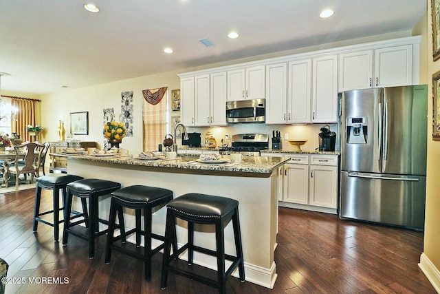 kitchen featuring dark hardwood / wood-style flooring, white cabinets, an island with sink, and appliances with stainless steel finishes