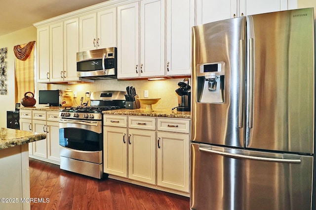 kitchen featuring light stone countertops, dark wood-type flooring, tasteful backsplash, white cabinets, and appliances with stainless steel finishes