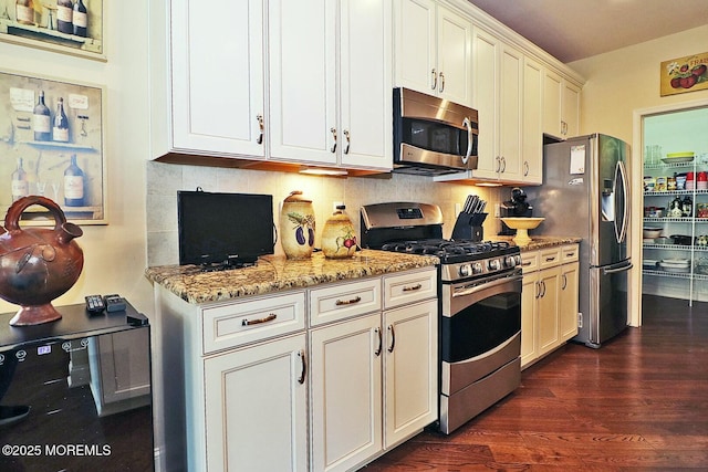 kitchen with dark wood-type flooring, light stone countertops, decorative backsplash, white cabinets, and appliances with stainless steel finishes