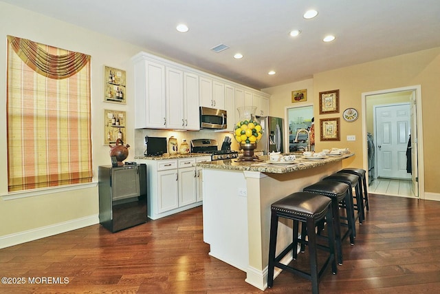 kitchen featuring appliances with stainless steel finishes, an island with sink, a kitchen bar, light stone counters, and white cabinets