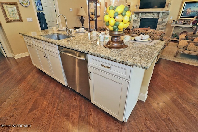 kitchen with dishwasher, sink, a center island with sink, white cabinetry, and a stone fireplace