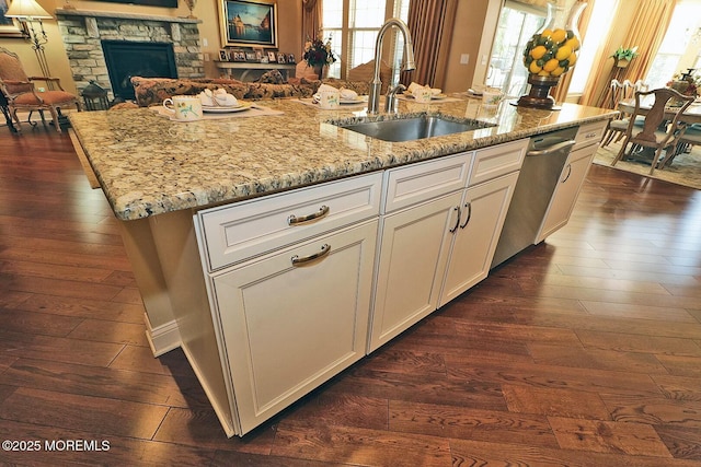 kitchen with sink, white cabinetry, stainless steel dishwasher, a kitchen island with sink, and a stone fireplace