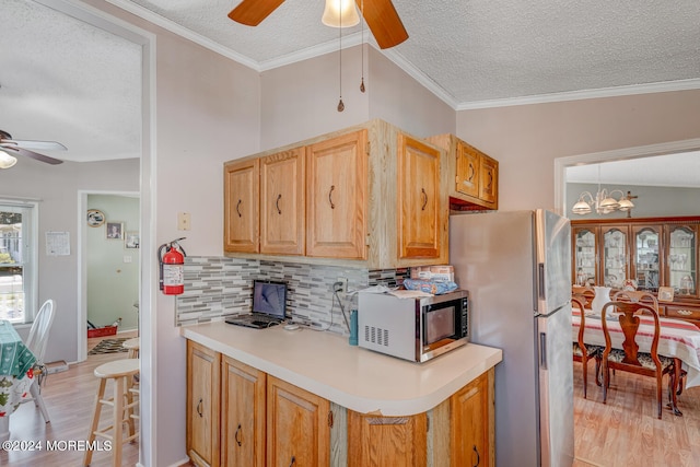 kitchen with stainless steel appliances, light wood-type flooring, a textured ceiling, decorative backsplash, and ornamental molding