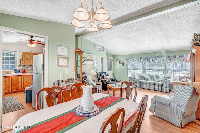 dining space featuring a textured ceiling, ceiling fan with notable chandelier, vaulted ceiling, and light wood-type flooring