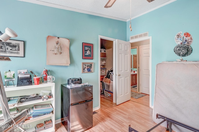 bedroom with stainless steel fridge, light wood-type flooring, a textured ceiling, ceiling fan, and crown molding