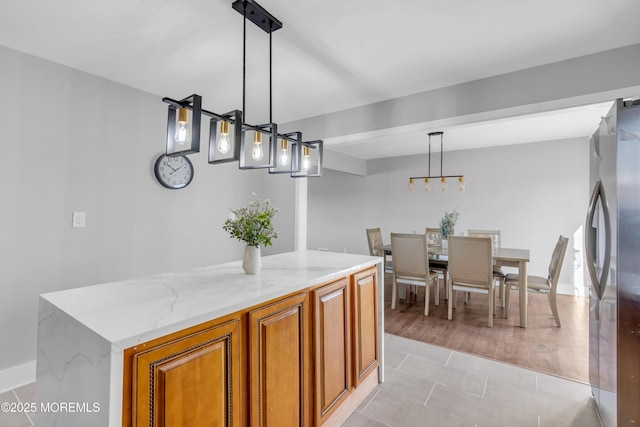 kitchen with stainless steel fridge, pendant lighting, light stone counters, a kitchen island, and light tile patterned flooring