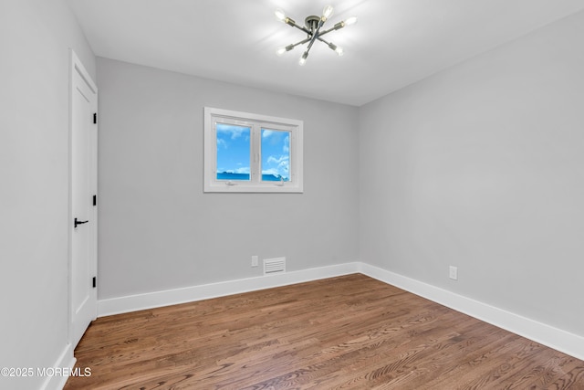 empty room with a notable chandelier and wood-type flooring