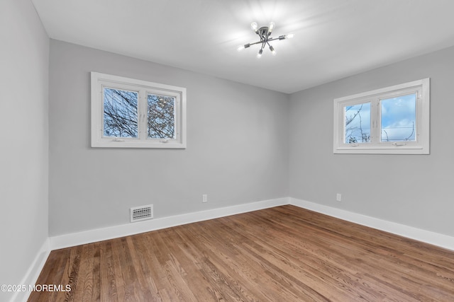 empty room featuring wood-type flooring and a chandelier