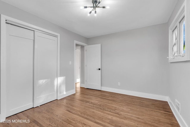 unfurnished bedroom featuring light wood-type flooring, a closet, and a chandelier