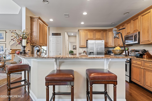 kitchen featuring sink, light stone counters, dark hardwood / wood-style floors, a kitchen bar, and appliances with stainless steel finishes