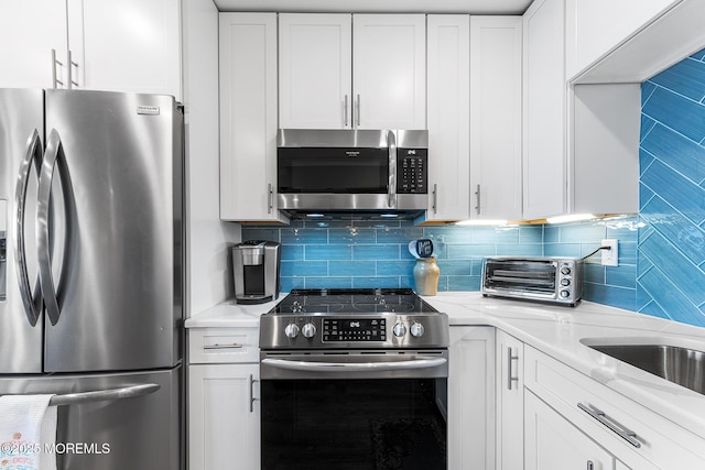 kitchen featuring stainless steel appliances, decorative backsplash, white cabinetry, and light stone countertops