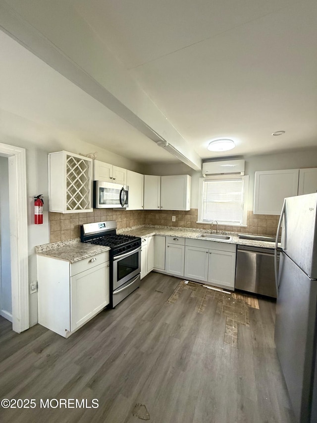 kitchen with dark wood-type flooring, a wall mounted AC, stainless steel appliances, white cabinets, and sink